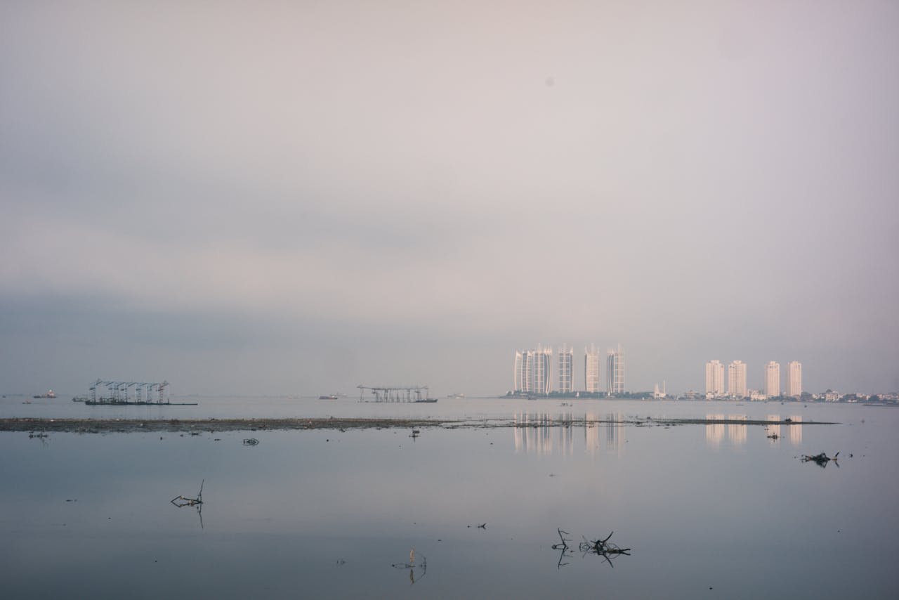Peaceful urban waterfront scene with skyline reflections during a misty morning in Indonesia.